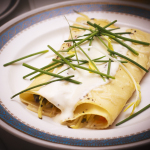 Rolled crepes with a white sauce and chives for garnish.